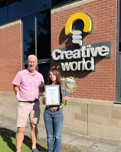 Woman holds certificate and flowers outside Creative World building