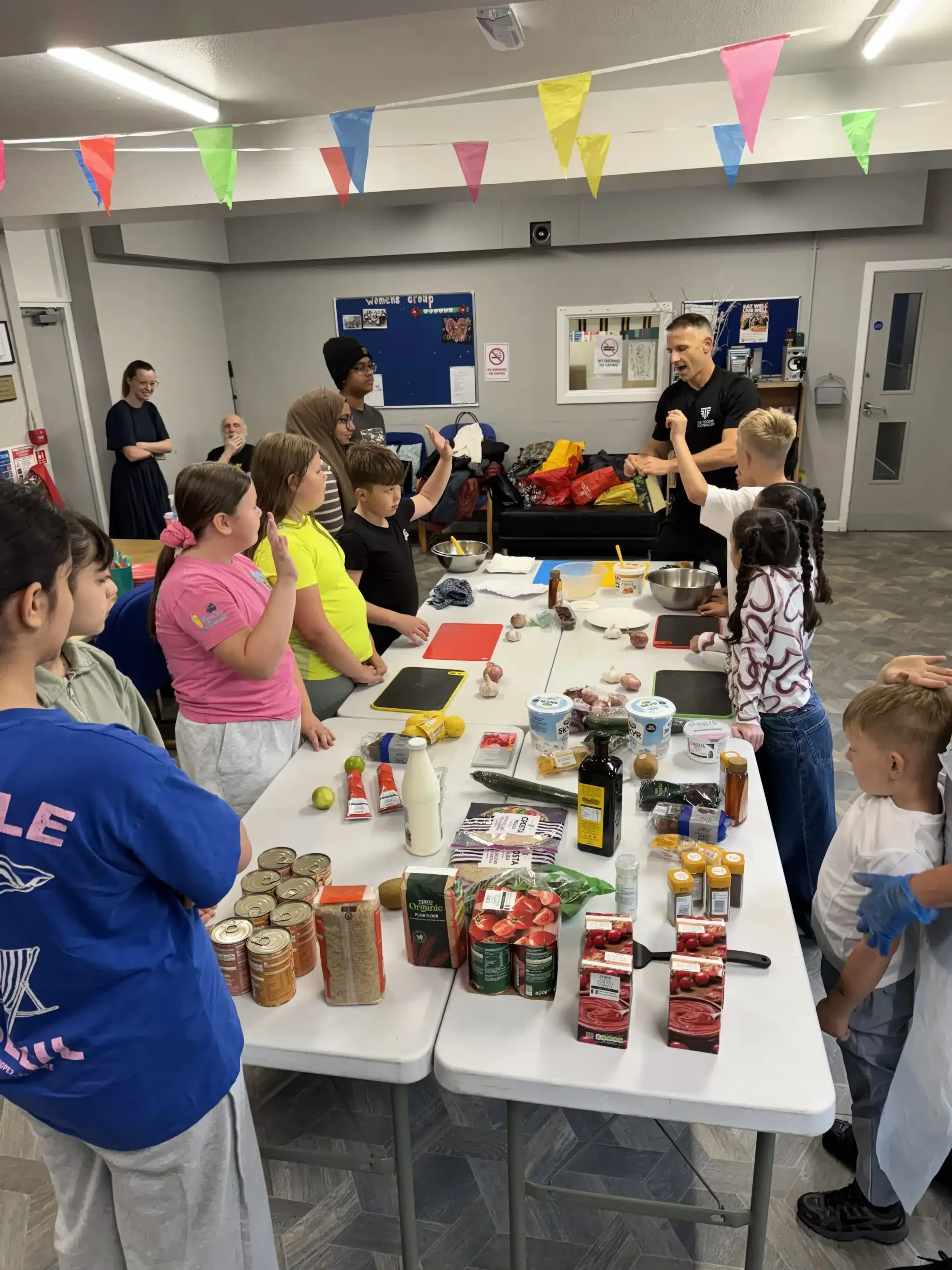 Children join a community cooking workshop around ingredient-filled tables