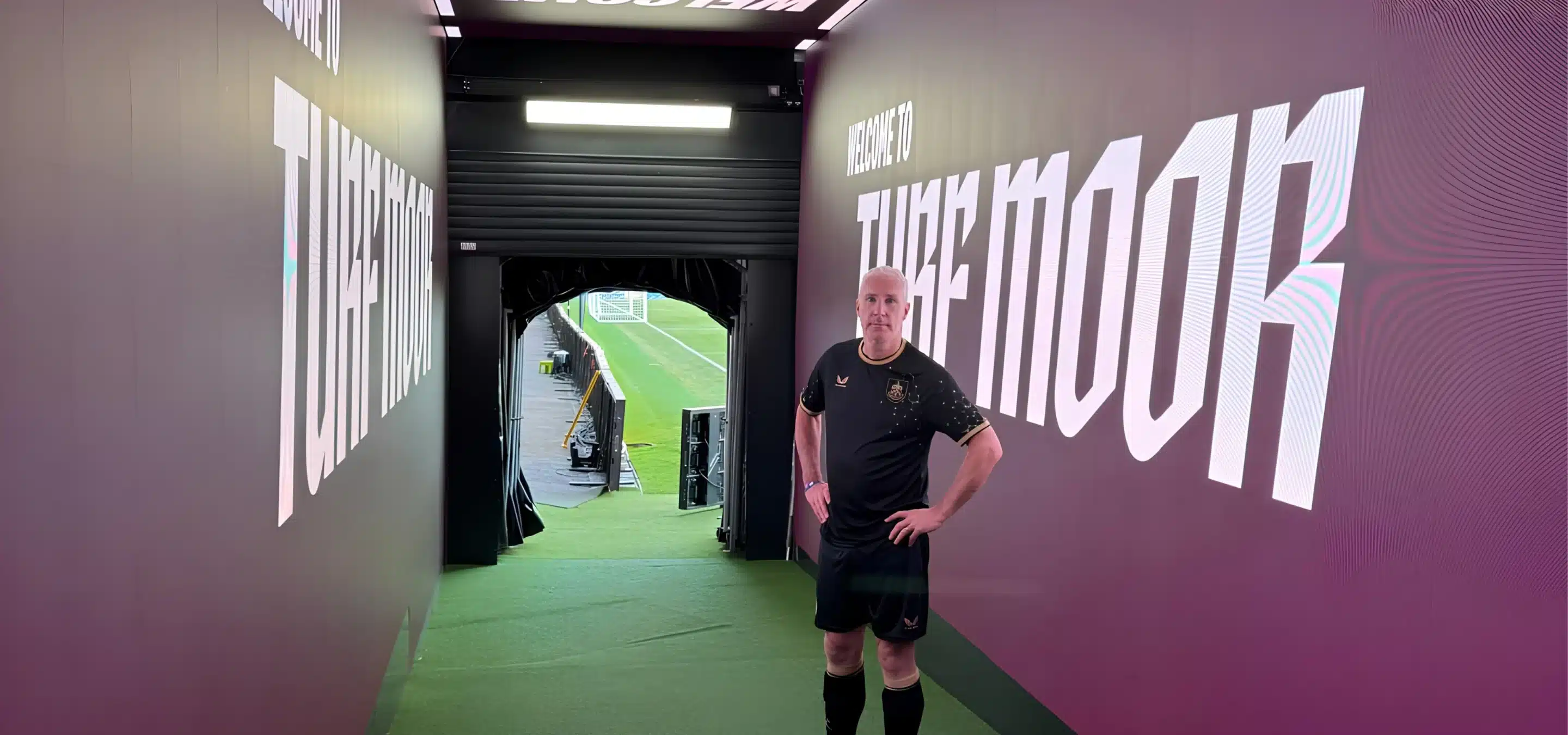 Footballer stands in stadium tunnel beside TikkTalk branding